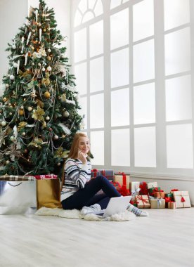 Genç kadın alışveriş online laptop rahat Noel iç. Sürü sarılmış hediye arasında süslü çam ağacının altında oturan kız. Xmas, bying kış satış için hazırlanıyor. Kopya alanı