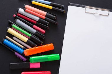 Siyah bir yüzeye, boş bir panonun yanına çeşitli renkli işaretler serpiştirilmiş, sanatsal ifadeler çağrıştırıyor. Çalışma alanı düzenli ve yaratıcılığa hazır görünüyor..