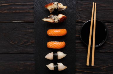 Suşi tabağı. Japon Gıda Restoran, unagi ve somon suşi koyu arka plan üzerinde. Yemek çubukları ve soya sosu ile ayarlayın. Siyah ahşap üzerine Üstten Görünüm