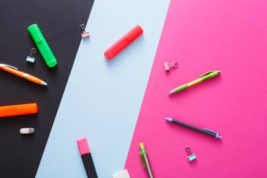 Kırtasiye eşyalarının canlı bir koleksiyonu siyah ve renkli bir arkaplan karşısında sergileniyor. Yazma araçları, ataçlar ve işaretleyiciler yaratıcılığa ilham vermek için stratejik olarak yerleştirilmiştir..