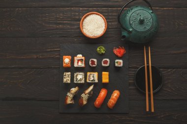 Japon restoranında renkli suşi ve dürüm tabakları, çaydanlık ve yemek çubukları üst görünümü, uzay kopyaları.