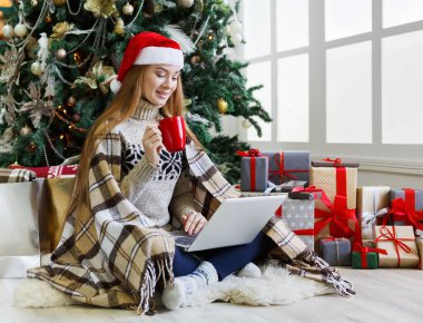 Yılbaşında internetten kahve alışverişi yapan genç bir kadın. Bir sürü hediye arasında süslenmiş köknar ağacının altında oturan kız. Xmas 'a hazırlanmak, kış satışlarında hile yapmak, kopyalama alanı