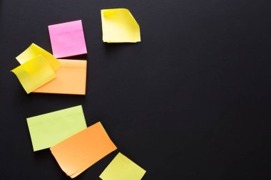 Değişik renkli yapışkan notlar, yaratıcılığı ve organizasyonu gösteren siyah bir yüzeye saçılmıştır. Notlar, proje ve görevler için beyin fırtınası, anımsatma ve planlama.