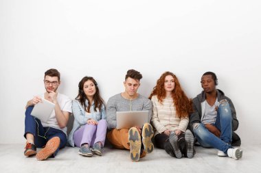 Çok ırklı uluslararası öğrenciler ellerinde aletlerle müzik dinliyorlar, içeride birlikte oturuyorlar. Kopya alanı olan beyaz arkaplanda modern eğitim