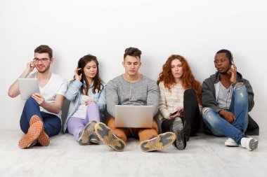 Çok ırklı uluslararası öğrenciler ellerinde aletlerle müzik dinliyorlar, içeride birlikte oturuyorlar. Kopya alanı olan beyaz arkaplanda modern eğitim