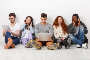 Çok ırklı uluslararası öğrenciler ellerinde aletlerle müzik dinliyorlar, içeride birlikte oturuyorlar. Kopya alanı olan beyaz arkaplanda modern eğitim