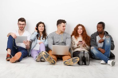 Çok ırklı uluslararası öğrenciler ellerinde aletlerle müzik dinliyorlar, içeride birlikte oturuyorlar. Kopya alanı olan beyaz arkaplanda modern eğitim