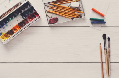 Çizim araçları, kırtasiye malzemeleri, işyeri sanatçı. Suluboya boya ve beyaz tahta masa, üstten görünüm, düz yatıyordu, boş kağıt alanı Kopyala