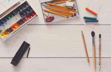 Çizim araçları, kırtasiye malzemeleri, işyeri sanatçı. Suluboya boya ve beyaz tahta masa, üstten görünüm, düz yatıyordu, boş kağıt alanı Kopyala