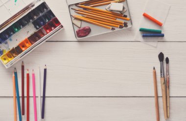 Çizim araçları, kırtasiye malzemeleri, işyeri sanatçı. Suluboya boya ve beyaz tahta masa, üstten görünüm, düz yatıyordu, boş kağıt alanı Kopyala