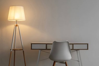 Beyaz boş sandalye, masa ve parıldayan lamba gri duvar arka planında ofis veya oturma odasında, hiç kimse. Kişisel izolasyon sırasında iş yeri covid-19 salgını, basit iç mekan, kopyalama alanı