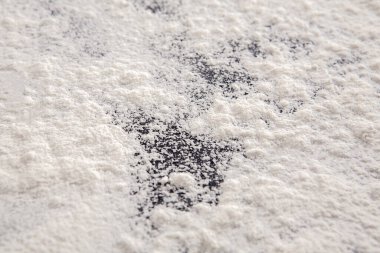 Yakın çekim, gölgelerin oluşturduğu hassas desenleri gösteren, koyu bir tezgahın üzerine yayılmış ince beyaz unu ortaya çıkarır..