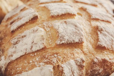 Yakından bakıldığında, altın-kahverengi bir ekmek sergileniyor. Kabuk güzelce desenlenmiş ve un ile tozlanmış, pişirme sürecini ve leziz dokusunu vurguluyor..