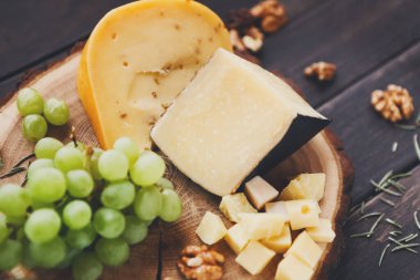 Peynir tabağı, doğal ahşap disk, tüm parçaları ve üzüm ve fındık, Natürmort, doğranmış peynir parmesan ve gouda ot alanı, arka plan kopyalama