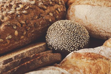 Çeşitli taze fırınlanmış ekmek türleri birlikte sıralanarak, sıcak ve davetkar bir atmosferde, diğer kırsal türler ve dokular arasında susam tohumlarıyla kaplı yuvarlak bir somun vurgulanıyor..