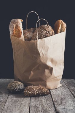 Kağıt torba siyah arka plan, rustik ahşap masada ekmek ürün yelpazesine sahip. Pastanede alışveriş