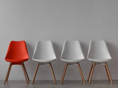 Üç boş beyaz sandalye ve ofiste ya da odada gri duvarda bir kırmızı. Basit minimalist iç mekan, hiç kimse, boş alan. İş edinme, liderlik ve iş hacmi covid-19 virüsü, model