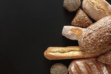 Ekmek, ekmek ve hamur işleri de dahil olmak üzere çeşitli zanaatkar ekmekler karanlık bir yüzeye güzelce yerleştirilmiştir. Dokuları ve renkleri her fırın meraklısı için mükemmel bir davet edici görüntü yaratır..