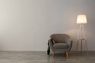 Ekoseli, parlak lambalı, gri duvarlı, oturma odasının arka planında basit bir koltuk. Minimalist, retro ve modern iç mekan, satılık ve kira için emlak, tasarım hakkında blog, model, serbest alan