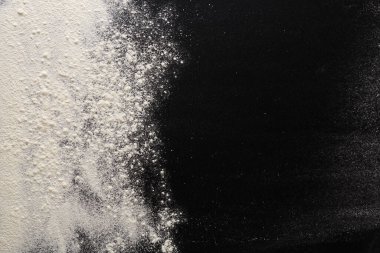 Beyaz un ve koyu dokulu yüzeyin dinamik bir karışımı keskin bir kontrast oluşturur. Un sanatsal bir şekilde dağılmış, pişirme ve pişirme elementlerini vurguluyor..