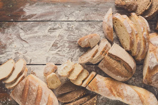 Ekmek çerçeve rustik ahşap arka plan üzerine dilimlenmiş, uzay kopyalayın. Kahverengi ve beyaz somun ve un üst çevresinde serpilir buğday unu ile kompozisyon görüntüleme.