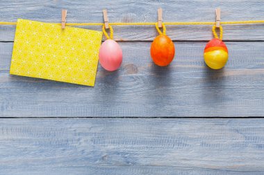 Canlı pastel Paskalya yumurtaları, sade ahşap bir arka planda dekoratif bir kartın üzerinde sarı bir sicimle kırpılır ve bayram için neşeli ve şen bir görüntü oluşturur..