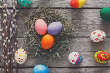 Kırsal bir ahşap masada farklı renklerde parlak renkli yumurtalar sergilenir..