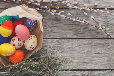 Canlı boyanmış Paskalya yumurtalarıyla dolu bir sepet kırsal ahşap bir masanın üzerinde duruyor. Dekoratif dallar ve saman, bahar renkleri yumurtaların etrafında belirdikçe neşeli atmosferi güçlendirir..