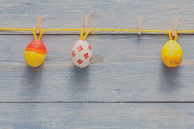 Parlak renkli Paskalya yumurtaları çamaşır mandallarıyla sarı bir ipe asılır. Ayar, şenlikli bahar dekorasyonları için mükemmel, kırsal ahşap bir arka plana sahip..