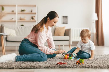 Young mother and her son playing with wooden stacking and sorting toy at home, sitting on floor carpet. Happy family playing and learning fine motor development