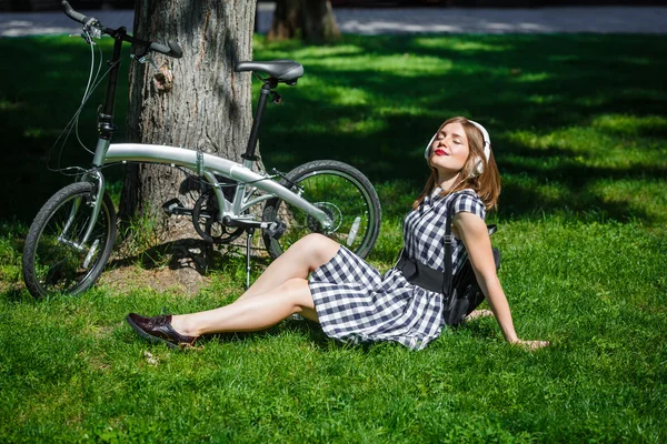 Mujer joven descansa cerca de la bicicleta en el parque — Foto de Stock