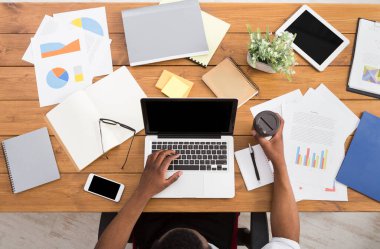 Office çalışma alanı üstten görünüm. Afrikalı-Amerikalı işadamı ahşap masa başında çalışan dizüstü bilgisayar ve çeşitli nesneleri her yerde kullanma