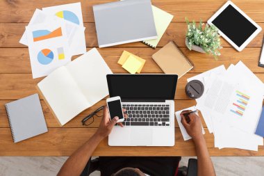 Office çalışma alanı üstten görünüm. Afrikalı-Amerikalı işadamı ahşap masa başında çalışan dizüstü bilgisayar ve çeşitli nesneleri her yerde kullanma