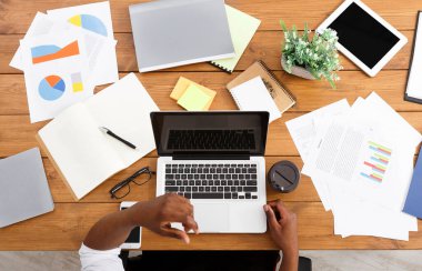 Ofis çalışma alanı üst görünüm kopya alanı ekranda. Tahta masada çalışan Afro-Amerikalı iş adamı, her yerde dizüstü bilgisayar ve çeşitli nesneler kullanıyor.