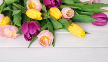 Bir grup lale çeşitli renklerde tahta bir yüzeye yerleştirilir. Çiçekler sarı, pembe ve yeşil yapraklı mor çiçekleri içerir. Bahar için parlak ve neşeli bir görünüm yaratırlar..