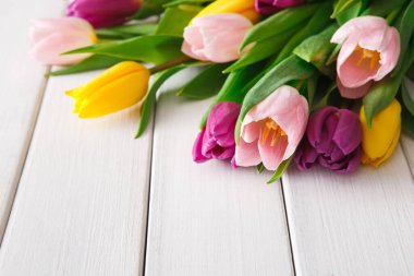 Farklı renklerde taze laleler beyaz ahşap bir masanın üzerinde toplanır. Çiçekler pembe, mor ve sarıdır. Bu düzenleme bahar ve tazeliğin özünü yakalar..