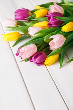 Pembe, mor ve sarı renkli çeşitli laleler beyaz ahşap bir yüzey üzerinde gelişigüzel düzenlenmiştir. Parlak çiçekler bahar mevsimini ve doğanın güzelliğini temsil eder..