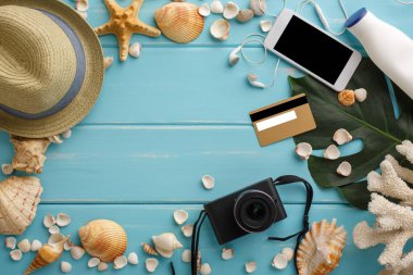 Mavi ahşap üzerinde tatil arka planı, fotokopi alanı olan üst manzara. Cep telefonu, fotoğraf makinesi, kredi kartı, şapka ve deniz kabukları.