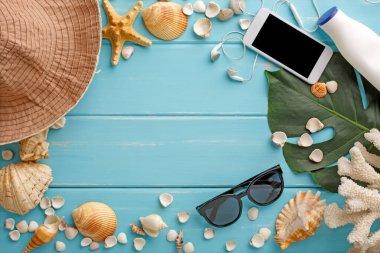 Mavi ahşap üzerinde tatil arka planı, fotokopi alanı olan üst manzara. Cep telefonu, güneş gözlüğü, şapka ve deniz kabukları.