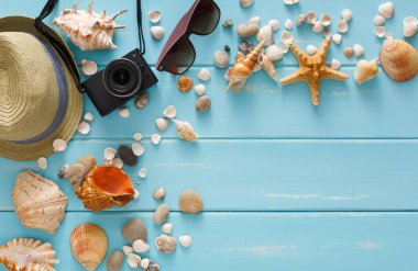 Mavi ahşap üzerinde tatil arka planı, fotokopi alanı olan üst manzara. Plaj aksesuarları, fotoğraf makinesi, güneş gözlüğü ve deniz kabukları.