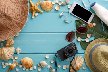 Mavi ahşap üzerinde tatil arka planı, fotokopi alanı olan üst manzara. Cep telefonu, fotoğraf makinesi, şapka ve deniz kabukları.