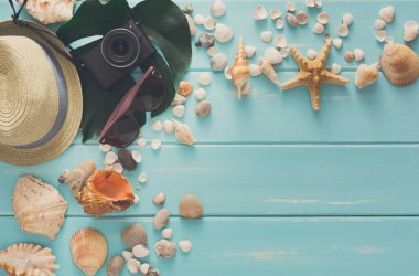 Mavi ahşap üzerinde tatil arka planı, fotokopi alanı olan üst manzara. Plaj aksesuarları, fotoğraf makinesi, güneş gözlüğü ve deniz kabukları.