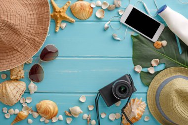 Mavi ahşap üzerinde tatil arka planı, fotokopi alanı olan üst manzara. Cep telefonu, fotoğraf makinesi, şapka ve deniz kabukları.