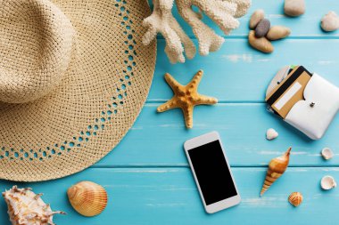 Mavi ahşap üzerinde tatil arka planı, fotokopi alanı olan üst manzara. Deniz kabukları ve hasır şapka. Akıllı telefondan bilet ayırtıyorum.