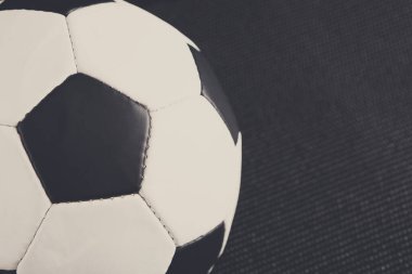 Bir futbol topu siyah bir yüzeye oturur, maç için hazırlanır. Top siyah ve beyaz panellerden yapılmıştır ve ayarı pratik veya oyun için kapalı bir spor ortamı önerir.