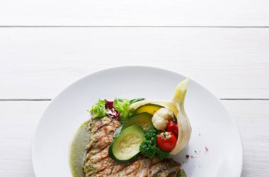 Bir tabak içinde ızgara balık, salatalık, kiraz domatesleri ve birkaç yaprak marul var. Ayar açık renkli bir yüzeyle parlak, yiyeceği açıkça gösteriyor..