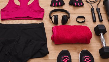 Ahşap zeminde bir spor eşyası koleksiyonu seriliyor. Anlaşmada bir spor sutyeni, şort, eldiven, kulaklık, havlu, ağırlık ve ayakkabılar yer alıyor. Bu kurulum etkin bir oturum için.