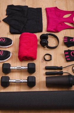 Ahşap zeminde ayakkabı, giysi, havlu, ağırlık, kulaklık ve aksesuarlarla bir egzersiz düzenlenir. Bu kurulum fitness eğitimi için hazır..