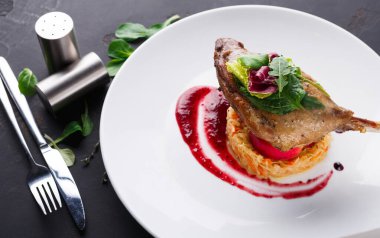 Kırmızı soslu eriştenin üzerine konmuş pişmiş ördek. Taze sebzeler ve otlar garnitür için eklenir. Ayarlar bir yemek odasının içinde, çatal bıçak ve tuzluğu gösteriyor..