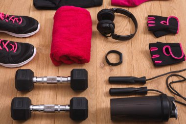 Ahşap yüzeyde farklı çalışma aletleri düzenlenir. Ayakkabılar, ağırlıklar, eldivenler, havlu, su şişesi ve kulaklık egzersiz için hazır..